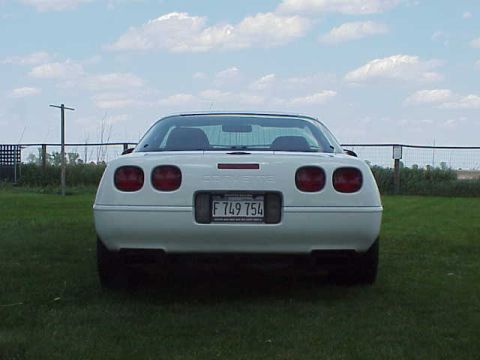 1994 Chevrolet Corvette - The rear of a white Chevrolet Corvette is shown parked on a grassy area under a cloudy sky.