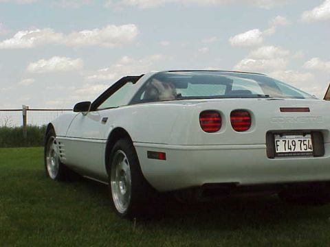 1994 Chevrolet Corvette - A white 1994 Chevrolet Corvette is parked on grass under a cloudy sky.