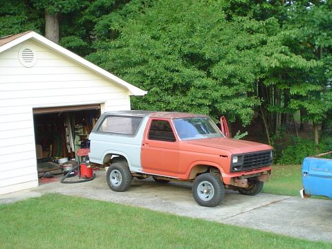 1981 Ford Bronco - This 1980 Ford Bronco, with its front end painted orange and the rear in gray, is parked outside a garage with its doors ajar.