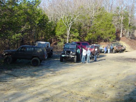 1974 Ford Bronco - Several off-road vehicles are parked together on a dirt path surrounded by trees.