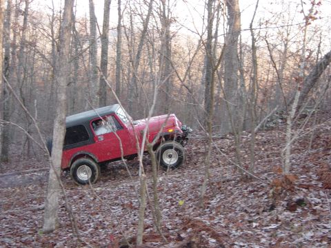 1974 Ford Bronco - Red Jeep CJ-7 navigates a wooded trail with its off-road suspension and tires.
