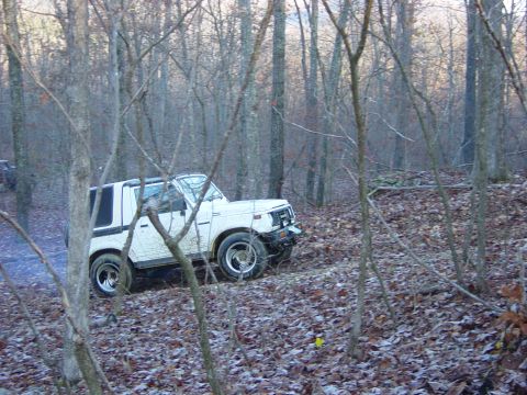 1974 Ford Bronco - A white Suzuki Samurai navigates a wooded area with dry leaves covering the ground.
