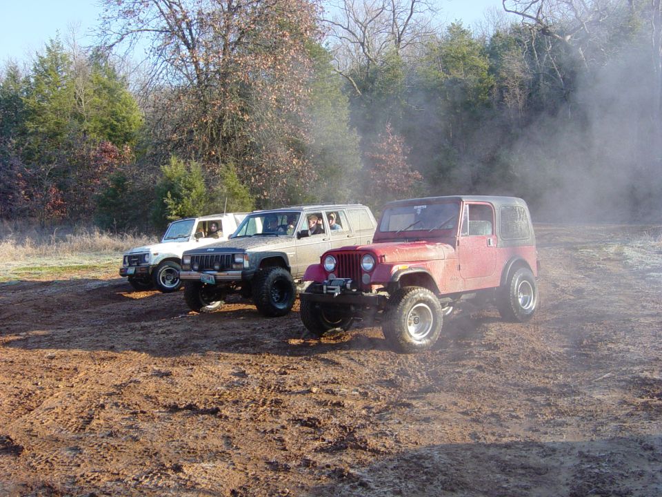 Three off-road vehicles parked on a dirt track with trees in the background