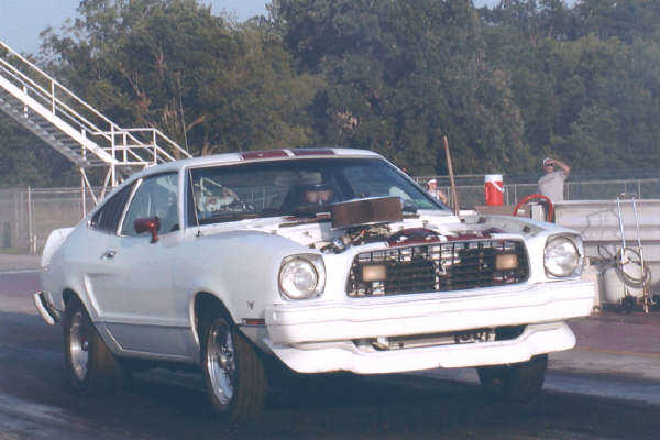White coupe with hood open, racing stripes, and custom wheels on a track