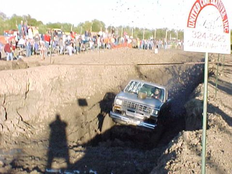 1987 Ford Ranger - A truck is shown driving through a muddy trench with a crowd watching in the distance.