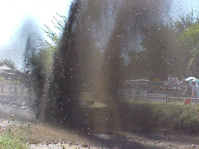 Huge mud and water spray at a mud bog event with spectators in background; no vehicle visible