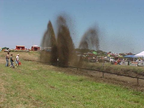 1987 Ford Ranger - Mud spray erupts from off-road vehicles during an event, with spectators and tents visible.
