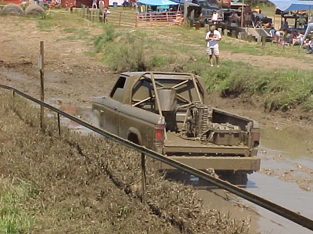 muddy pickup truck with roll cage driving through a mud pit