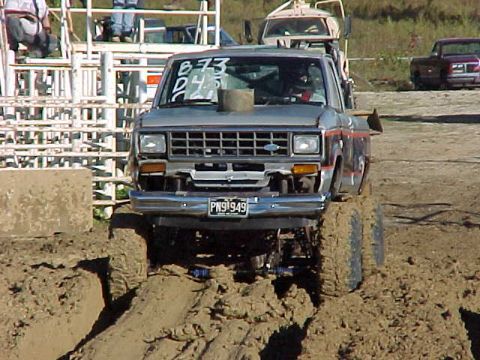 1987 Ford Ranger - Mud-covered 1987 Ford Ranger navigates a muddy track with other vehicles in the background.