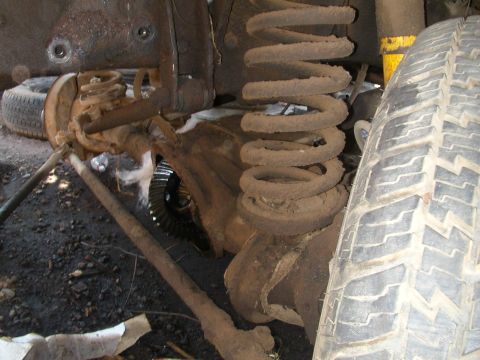 1993 Ford Bronco - This photo shows the rusty front axle, suspension, and tire of a vehicle, likely taken during maintenance or repair.
