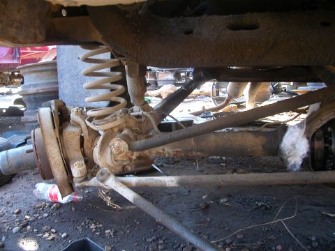 1993 Ford Bronco - Close-up view of a vehicle's front axle assembly, including the coil spring and shock absorber, in a junkyard setting.