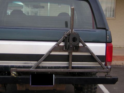 1995 Ford Bronco - Rear view of a dark green and white Ford Bronco, equipped with a custom-built spare tire carrier attached to the bumper.