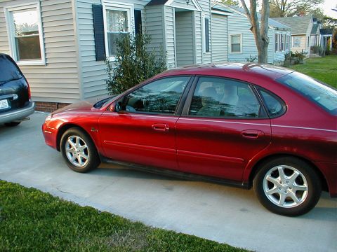 2000 Ford Taurus - Side view of a red 2000 Ford Taurus parked on a driveway with a house in the background.