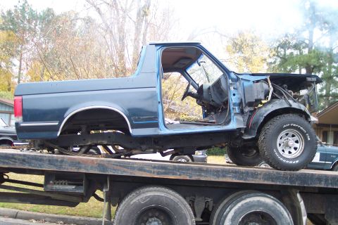 1989 Ford Bronco - 1989 Ford Bronco body being transported on a flatbed truck, stripped of many parts.