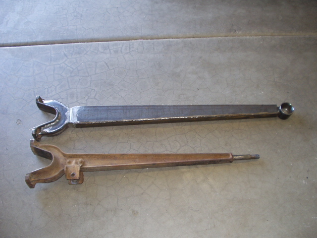 Two forked metal shift fork parts on concrete, one polished, one rusty