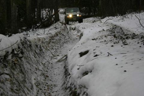 2003 Jeep TJ - A Jeep Wrangler navigates a challenging snowy path in a wooded area.