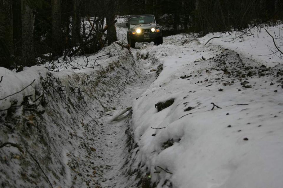 Jeep Wrangler driving through a snowy ditch in a forest