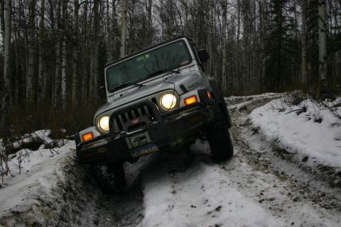 2003 Jeep TJ - A silver 2003 Jeep TJ navigates a challenging snowy path through a dense forest.