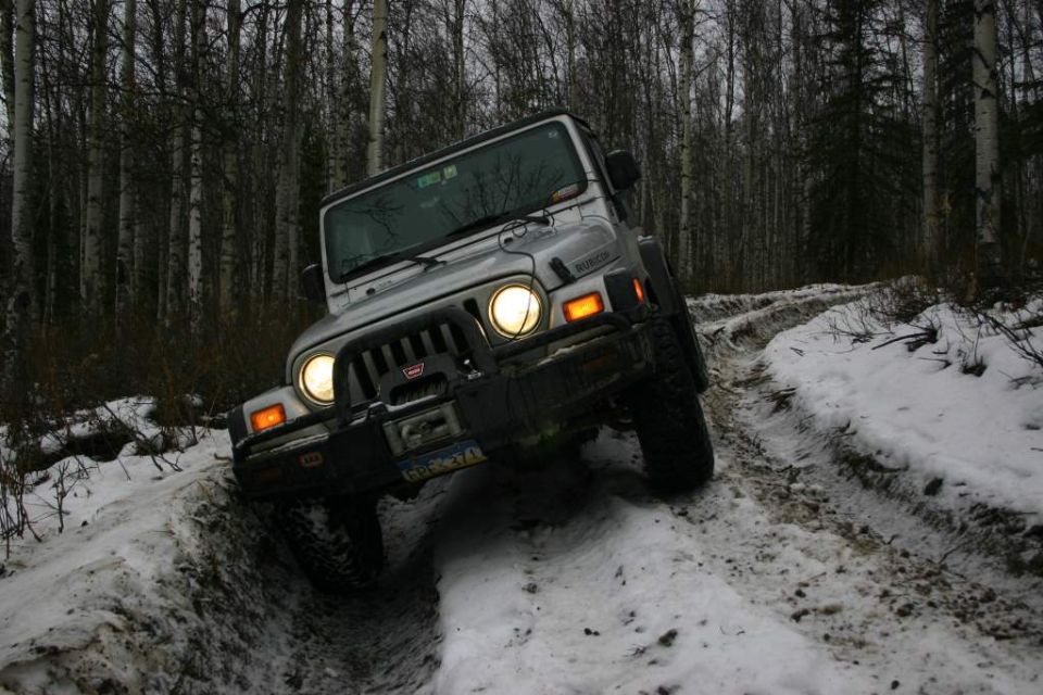 Silver 2003 Jeep TJ driving on a snowy trail in a forest