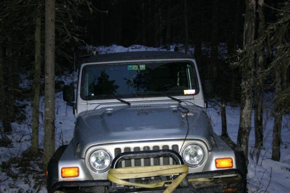 Silver Jeep TJ in snowy woods, front view. Has a yellow tow strap across the grille