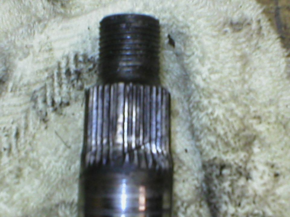 Close-up of a damaged metal shaft with splines and threaded end, resting on a textured cloth