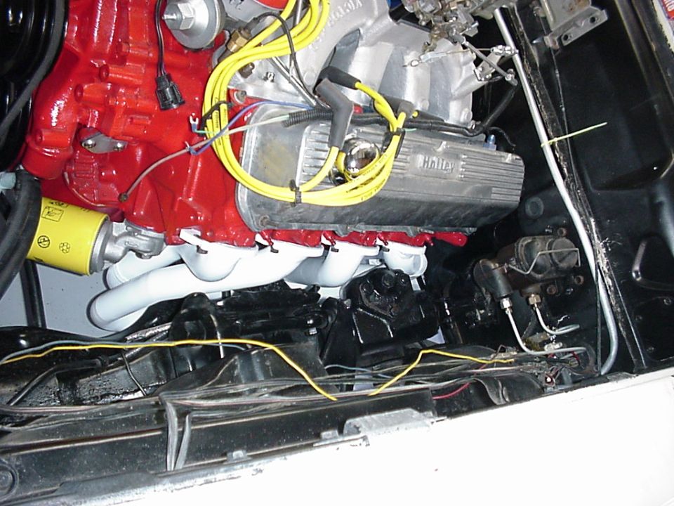 Red V8 engine with Holley valve cover, yellow plug wires and white exhaust manifold