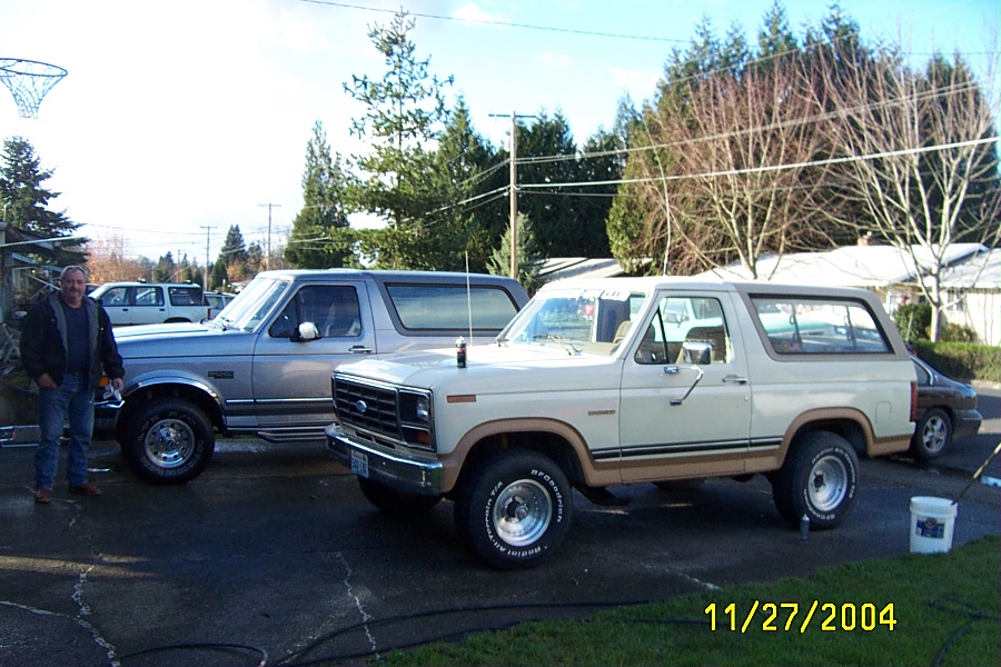 Tan two-tone Ford Bronco SUV parked in driveway with a gray pickup behind it