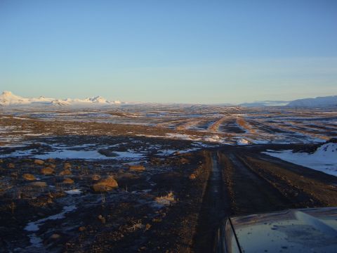1996 Ford Bronco - Driving on a dirt road through a vast, snow-dusted terrain with distant mountains.