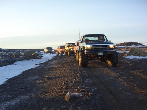 1996 Ford Bronco - A convoy of off-road vehicles travels along a desolate, rocky path under a clear sky.
