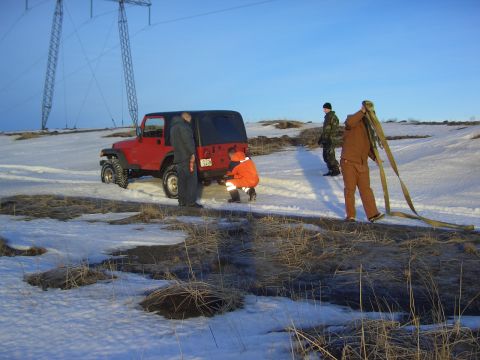 1996 Ford Bronco - People are gathered around the rear of a red Jeep Wrangler in a snowy, open area with power lines overhead.