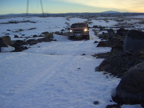 1996 Ford Bronco - A red SUV navigates a snowy path with large rocks and power lines in the background.