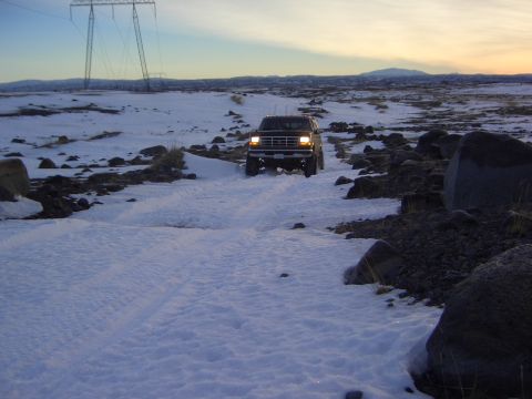 1996 Ford Bronco - A 1996 Ford Bronco navigates a snowy and rocky landscape at dusk.