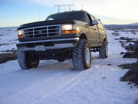 1996 Ford Bronco - This lifted Ford F-Series truck is equipped with large off-road tires and is driving on a snowy path.