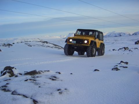 1996 Ford Bronco - A yellow off-road vehicle navigates a snow-covered terrain under a bright sky.
