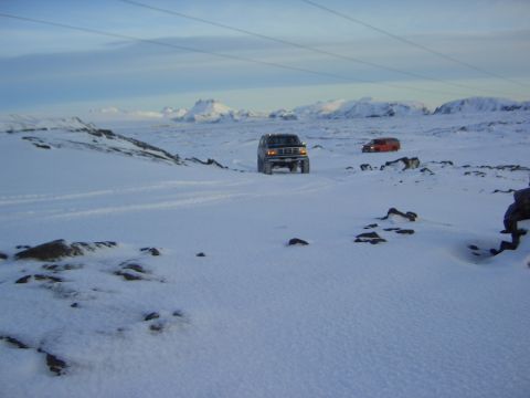 1996 Ford Bronco - A dark SUV navigates a snow-covered landscape with mountains visible in the distance, suggesting a winter expedition.