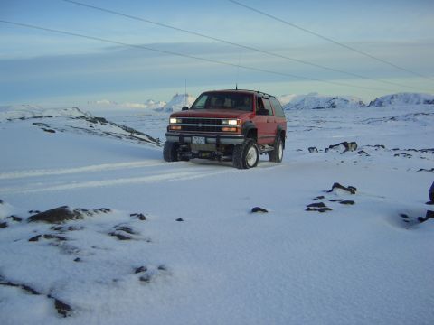 1996 Ford Bronco - This red SUV is driving through a snowy, mountainous terrain under a clear sky.