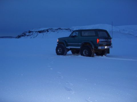 1996 Ford Bronco - A green 1996 Ford Bronco navigates a snow-covered terrain under a twilight sky.
