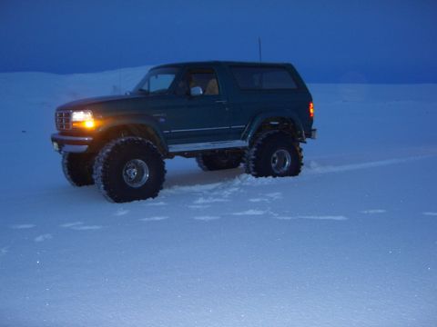 1996 Ford Bronco - 1996 Ford Bronco with oversized tires parked in a snowy field at dusk.