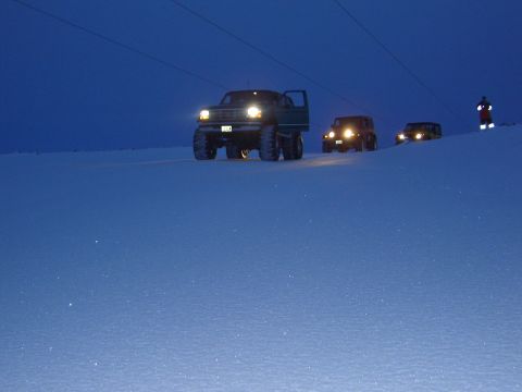 1996 Ford Bronco - Several vehicles drive through a snowy landscape under a dark blue sky, with one person visible in the distance.