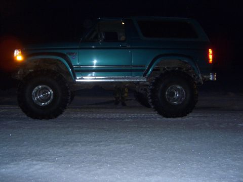 1996 Ford Bronco - A teal 1996 Ford Bronco with oversized tires sits on a snowy surface at night.