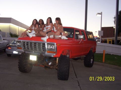 1989 Ford Bronco - Four women pose on the hood of a lifted red SUV, with a silver car visible in the background.