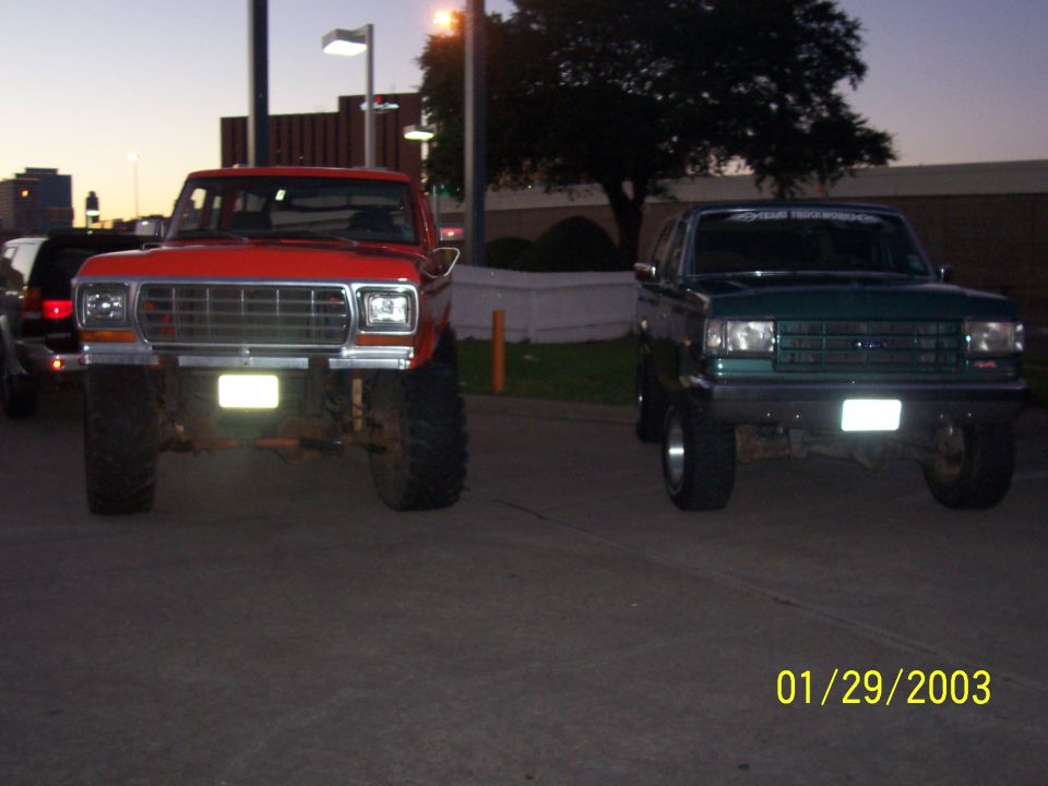 Red lifted Ford truck and green lifted Bronco parked side by side at dusk, front view