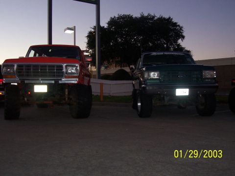 1989 Ford Bronco - Two lifted pickup trucks parked side-by-side at dusk.