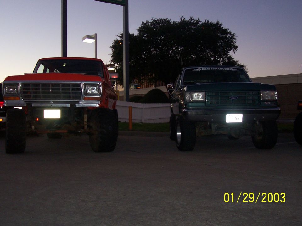 Lifted orange bullnose Ford and green Bronco parked front-on at dusk