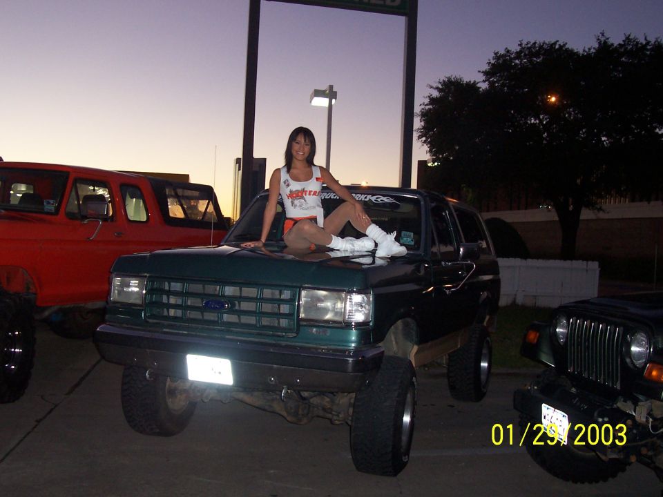 Lifted dark green Ford Bronco at dusk with a person seated on the hood