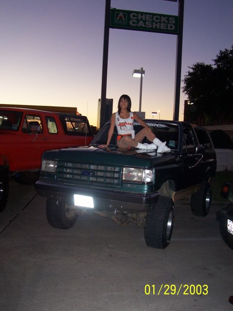 1989 Ford Bronco - A woman poses on the hood of a lifted green Ford Bronco in front of a 'Checks Cashed' sign.