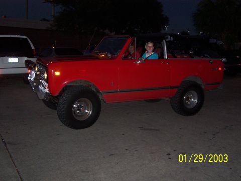 1989 Ford Bronco - A red convertible SUV is seen from the side with two occupants in the front seats.
