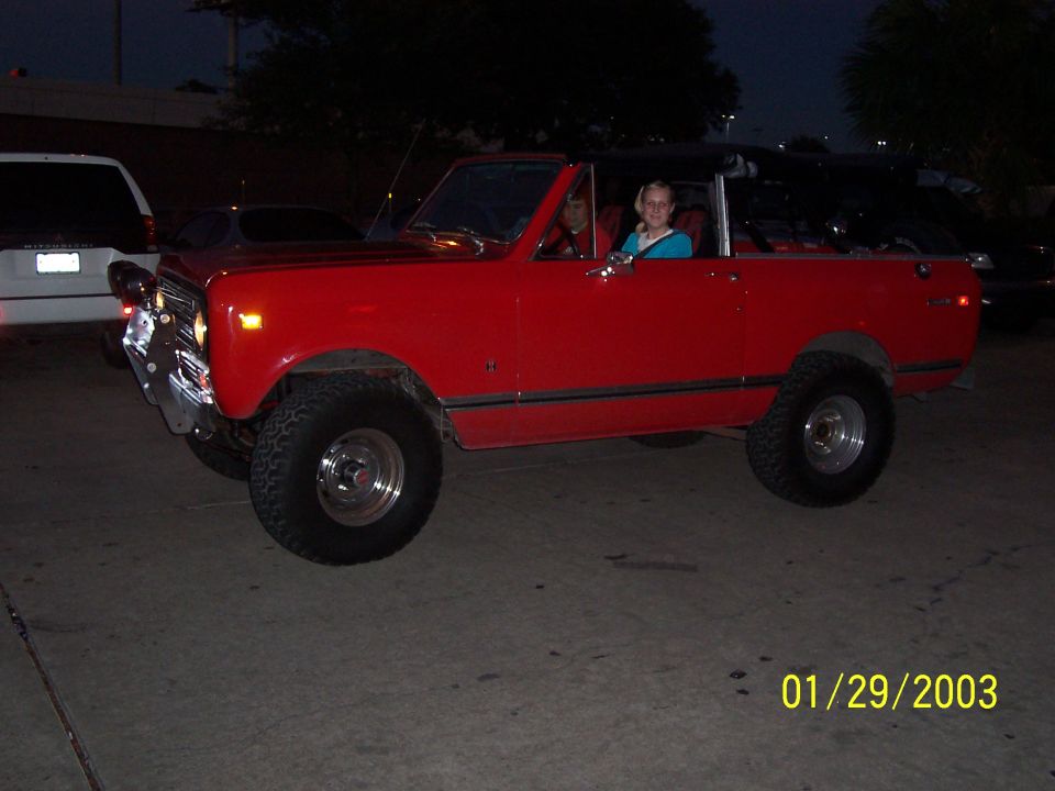 Red lifted International Scout with top removed and chrome wheels in a parking lot at dusk
