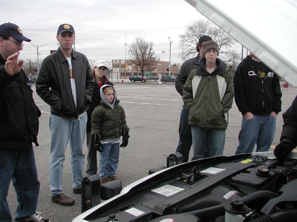 White 1987 Lincoln Town Car with hood open, showing engine bay. Several people stand around it