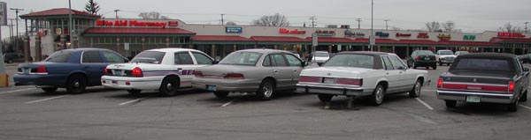Several sedans parked in a lot, including a white car with a black vinyl roof and a black sedan